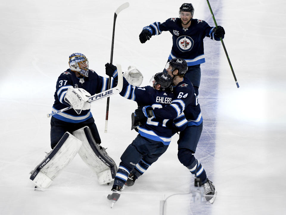 Winnipeg Jets' Nikolaj Ehlers (27) celebrates his game-winning goal with teammates Connor Hellebuyck (37), Dylan DeMelo (2) and Logan Stanley (64) in the first overtime period of an NHL hockey Stanley Cup playoff game against the Edmonton Oilers, Sunday, May 23, 2021, in Winnipeg, Manitoba. (Fred Greenslade/The Canadian Press via AP)