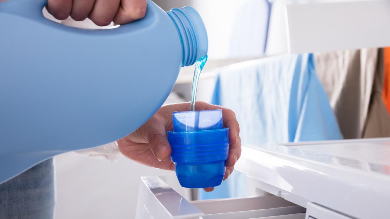 Close-up Of A Person's Hand Pouring Detergent In Lid.