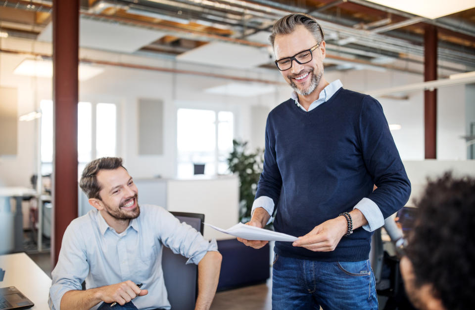 Mature businessman holding a document talking with colleagues sitting in office. Team having meeting over new business plan in the office.