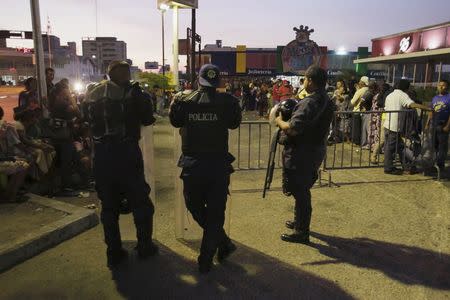 Police officers stand guard next to people waiting in a line for the opening hour to buy staple items outside a supermarket in Maracaibo August 8, 2015. REUTERS/Isaac Urrutia