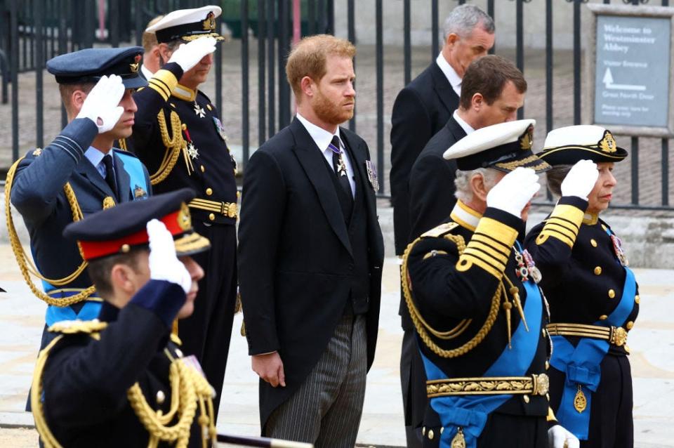 Prince Harry, wearing a morning suit, stands with royal family members wearing military uniforms