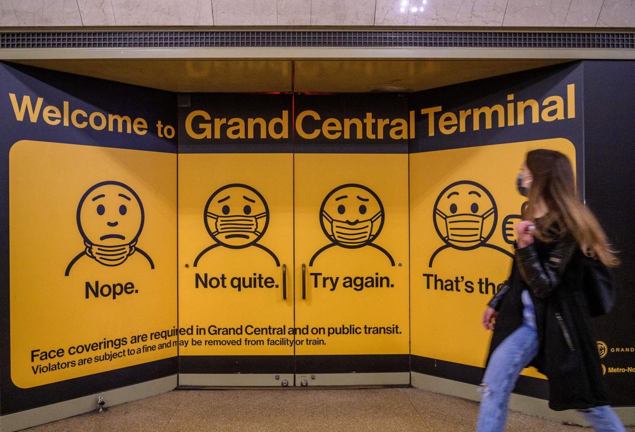 A woman wearing a face mask walks past posters explaining how to wear a mask at Grand Central Terminal train station in midtown Manhattan, New York.