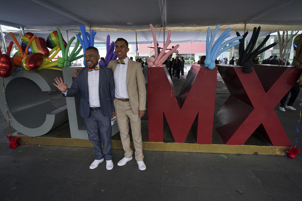 A same sex couple pose for a photo in front the city's logo prior to a mass wedding ceremony organized by city authorities as part of the LGBT pride month celebrations, in Mexico City, Friday, June 24, 2022. (AP Photo/Fernando Llano)