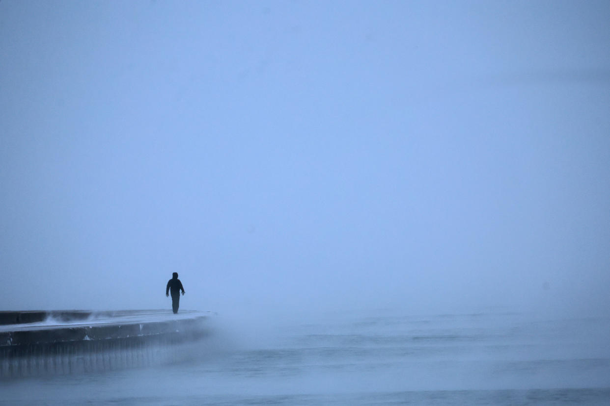 A man walks along Lake Michigan at sunrise, though the sun cannot be seen.