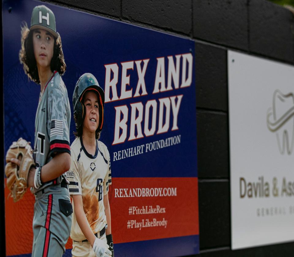 A billboard is seen on the fence walking into the baseball field area at Buchholz High School for the Rex and Brody Foundation Thursday, April 14, 2022, at Buchholz High School, in Gainesville, Florida. The Reinhart brothers were tragically killed by their father in a murder-suicide in May 2021. The boys were very active in baseball, and so their mother Minde Reinhart set up the Rex and Brody Foundation in their name, to help fund youth baseball players who might not be able to afford it. It also helps fund scholarships and facility upgrades for local ball fields. Minde Reinhart also threw out the first pitch before the game.