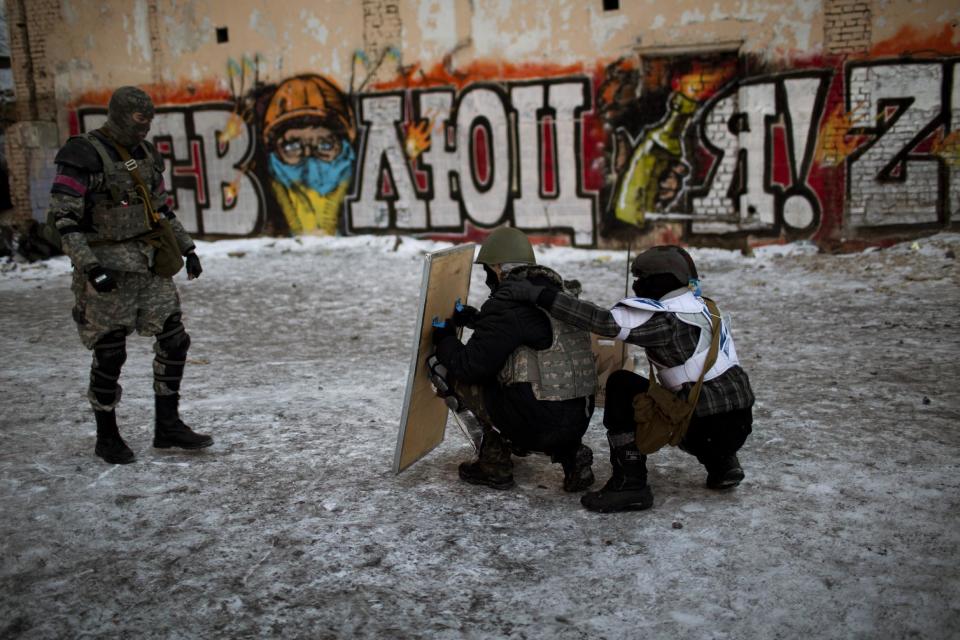 Two opposition supporters learn how to protect themselves behind a shield as they receive training near Kiev's Independence Square, the epicenter of the country's current unrest, Ukraine, Friday, Jan. 31, 2014. Police on Friday opened an investigation into the kidnapping of an opposition activist, who said he was held captive for more than a week and tortured in the latest in a string of mysterious attacks on anti-government protesters in the two-month-long political crisis. The graffiti reads in Ukrainian "Revolution". (AP Photo/Emilio Morenatti)