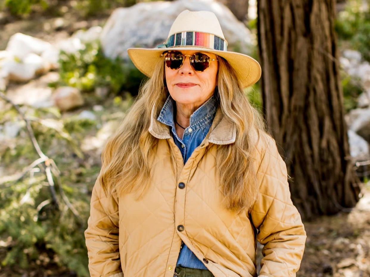 woman in a hat sunglasses and coats stands in a forest