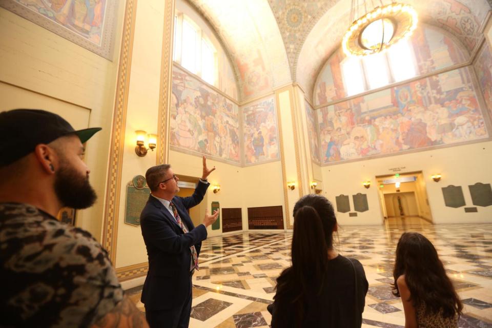 A man standing in a room with high ceilings gestures to others