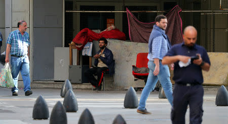 A homeless man sits outside an out-of business store as people walk by in Buenos Aires' financial district, Argentina October 18, 2018. Picture taken October 18, 2018. REUTERS/Marcos Brindicci