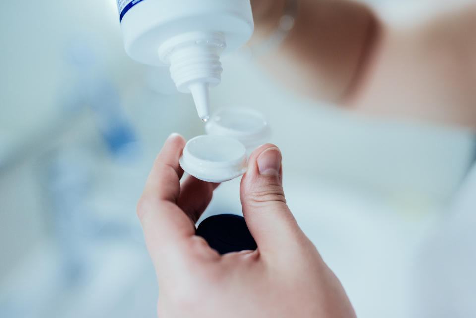 Woman putting cleaning dilution into contact lens case.