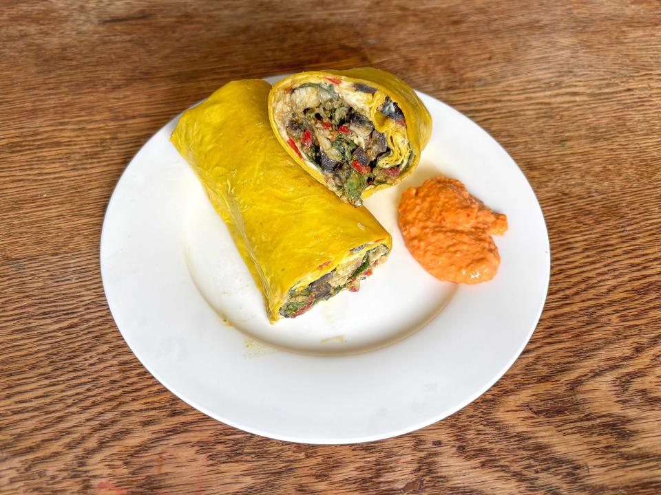 A white plate with two wraps with yellow tortillas next to a small pool of orange dipping sauce.