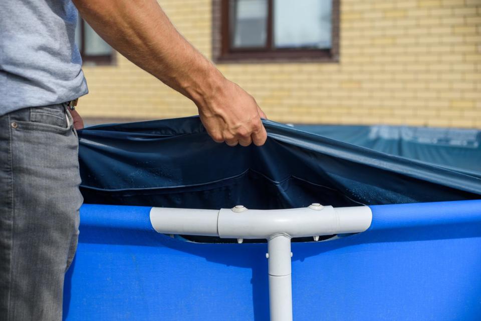 A man pulls up a cover over an above-ground swimming pool. 