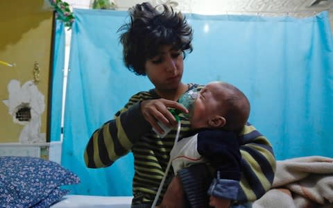 A Syrian boy holds an oxygen mask over the face of an infant at a make-shift hospital following a reported gas attack on the rebel-held besieged town of Douma - Credit: AFP