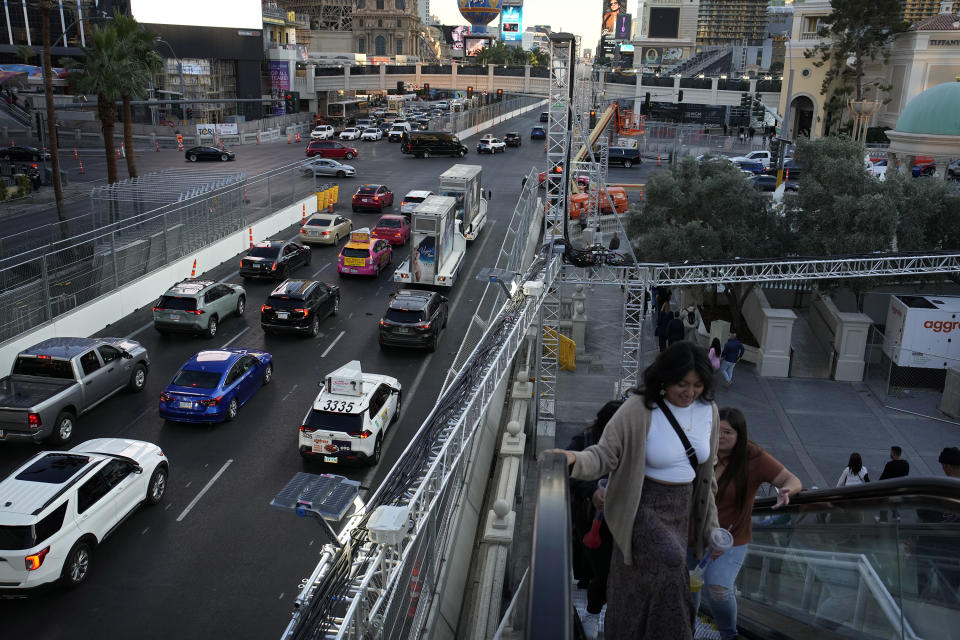 Pedestrians take an escalator along the Las Vegas Strip beside rigging and fencing installed ahead of the Las Vegas Formula One Grand Prix auto race Friday, Nov. 10, 2023, in Las Vegas. (AP Photo/John Locher)