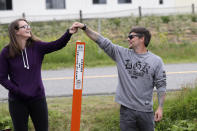 In this photo taken May 17, 2020, Kris Browning, left, stands in Canada and holds hands with her husband, Tim Browning, in the U.S., after posing for a photo at the border near Lynden, Wash. With the border closed to nonessential travel amid the global pandemic, families and couples across the continent have found themselves cut off from loved ones on the other side. (AP Photo/Elaine Thompson)