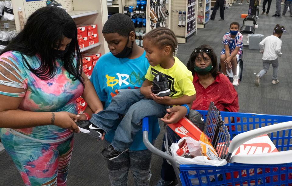 Caitlin Coker fits shoes on King Jackson as Deandre Batts and Diana Sneed watch. The family was one of four families that received a $1,000 gift card from Academy Sports and Outdoors last December. The family has been able to move into a new home.