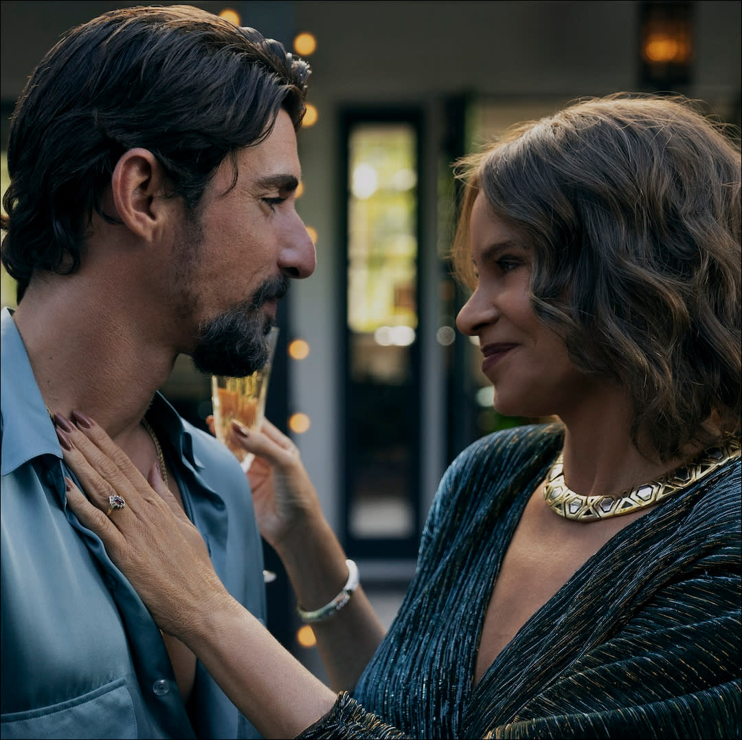  A man (Alberto Guerra as Dario) gazes at a woman (Sofia Vergara as Griselda) as she places a hand on his chest and holds a glass of champagne during a party. 