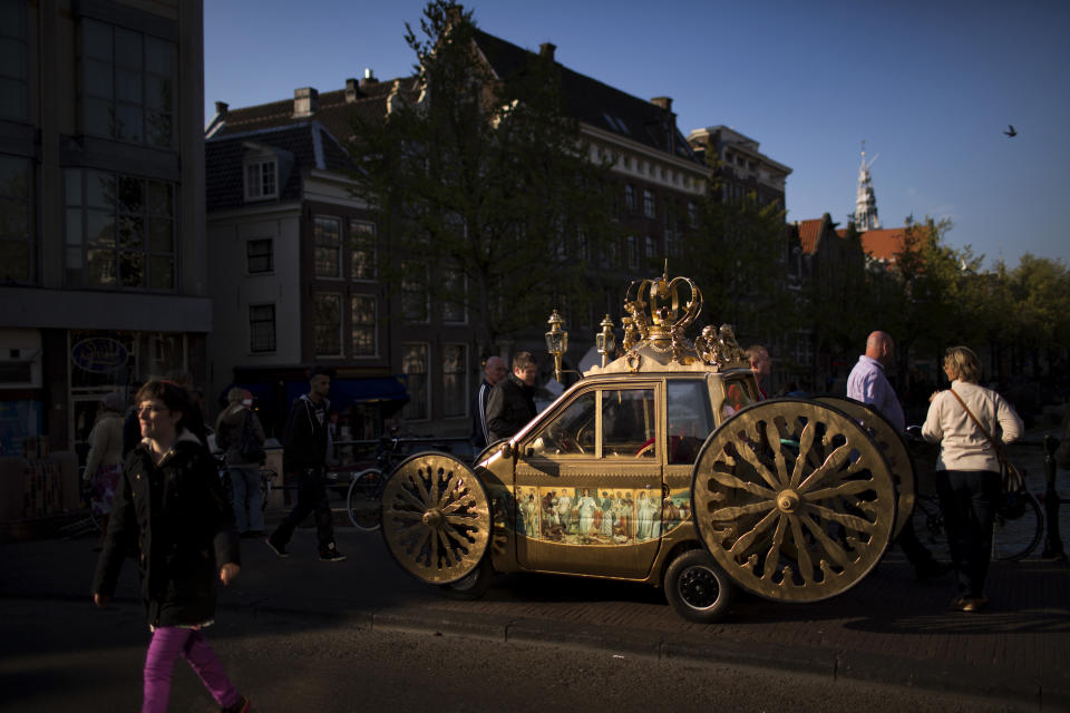 People walk past a car decorated as a royal carriage in downtown Amsterdam, Netherlands Sunday, April 28, 2013. Queen Beatrix announced she will relinquish the crown on April 30, 2013, after 33 years of reign, leaving the monarchy to her son Crown Prince Willem Alexander. (AP Photo/Emilio Morenatti)