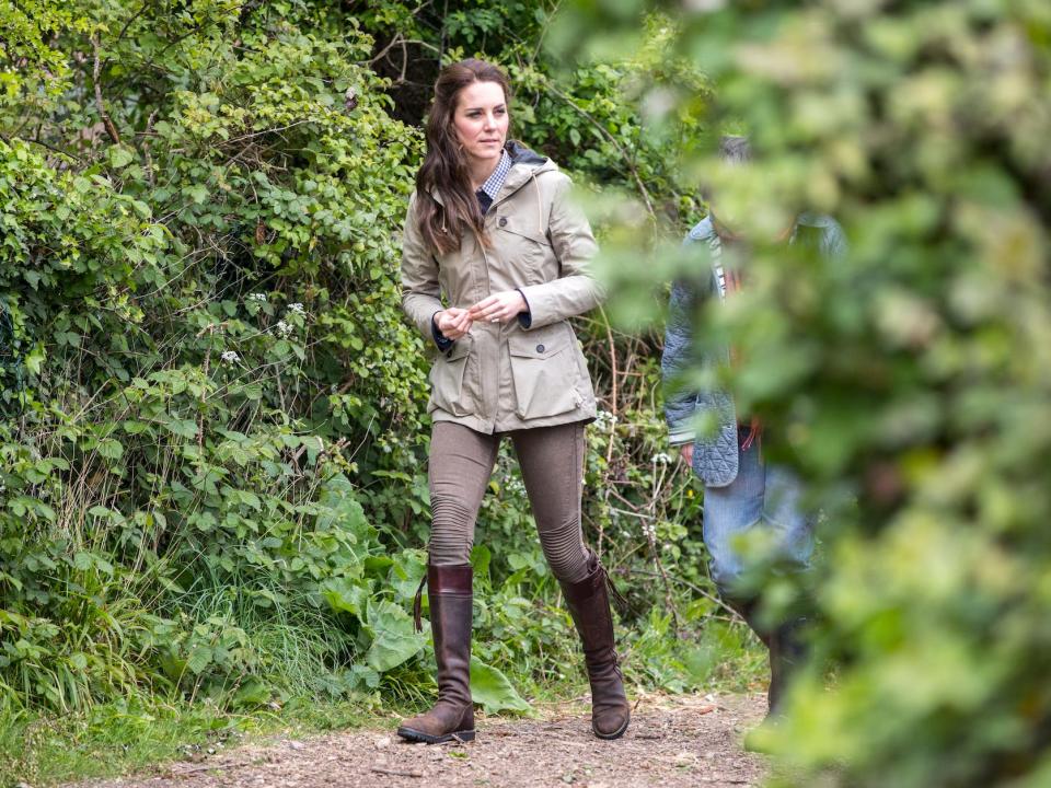 Kate Middleton walking through a wooded path in boots and a jacket.