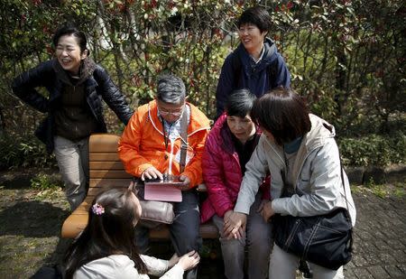 61-year-old Masahiko Sato (wearing an orange jacket), who has become a kind of "poster boy" for Japan's growing number of people with dementia, and a 62-year-old woman (wearing a pink jacket), who did not want to give her name and diagnosed with dementia about decade ago, are surrounded by their supporters during a cherry blossom viewing event at Omiya park in Omiya, north of Tokyo, Japan, March 27, 2016. REUTERS/Issei Kato