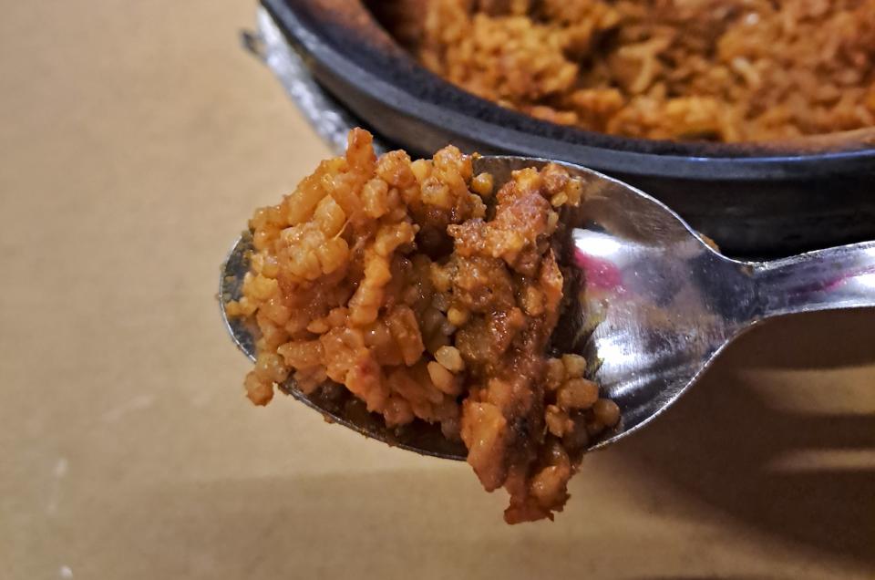 A scoop of claypot-cooked chicken rice on a metal spoon.