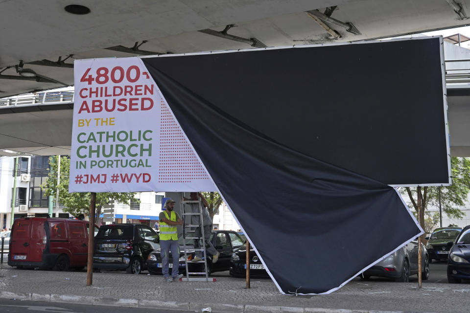 A municipal worker takes down a protest billboard against alleged child abuse by the catholic church in Alges, just outside Lisbon, Portugal, Wednesday, Aug. 2, 2023. Pope Francis has started his five-day pastoral visit to Portugal that includes his participation at the 37th World Youth Day, and a pilgrimage to the holy shrine of Fatima. (AP Photo/Ana Brigida)