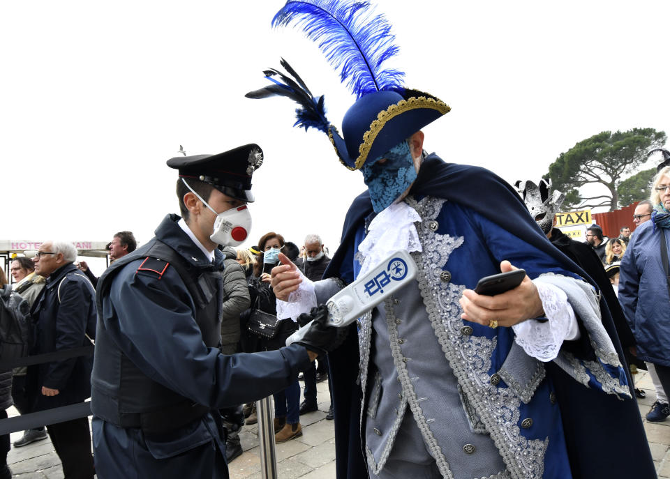 A policeman wearing a sanitary masks controls with a metal detector a reveler in Venice, Sunday, Feb. 23, 2020. Italian authorities have announced they are shutting down Venice's famed carnival events in a bid to stop the spread of the novel virus, as numbers of infected persons in the country have soared to at least 133, the largest amount of cases outside Asia. (AP Photo/Luigi Costantini)