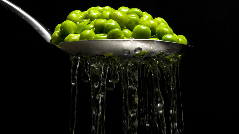 Slotted spoon of peas with water draining from it