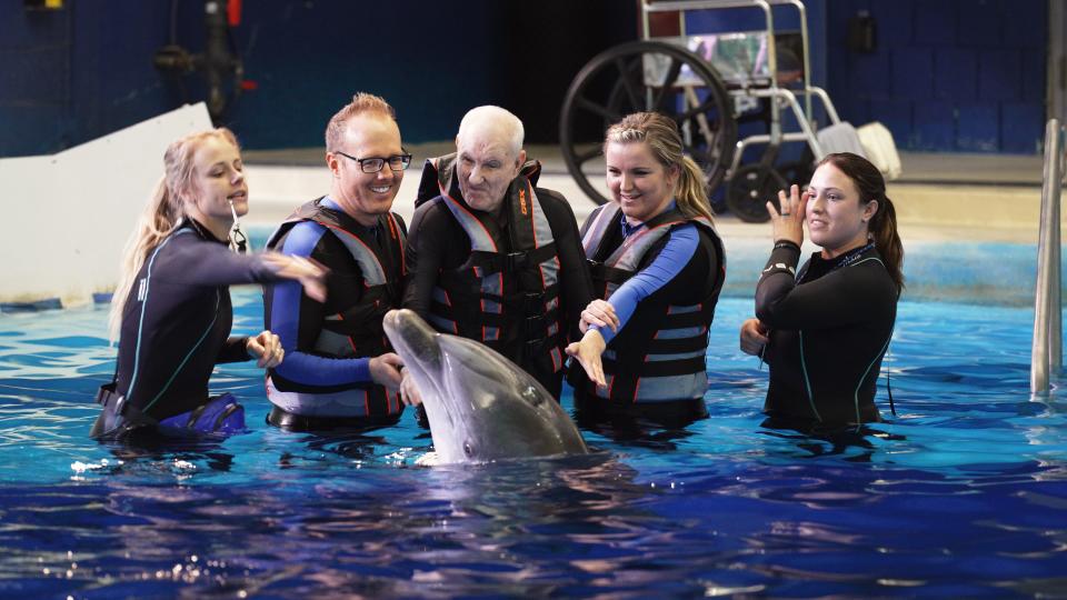 Ricky, 74, pets a dolphin at the Indianapolis Zoo with Dr. Gregory Taylor, Logan Long and two dolphin trainers at his side during his zoo trip made possible by Physicians for Wishes.