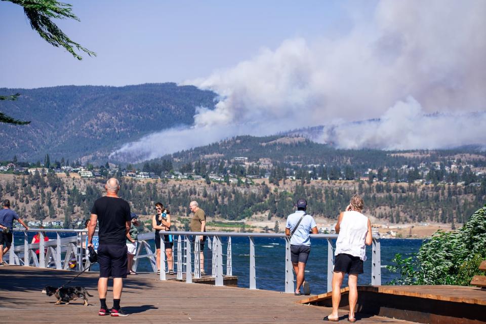 People in Pandosy Waterfront Park in Kelowna watch McDougall Creek wildfire burning in West Kelowna amid strong winds on Aug. 18, 2023.