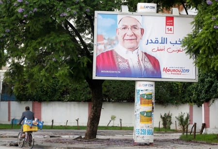 A man rides a bicycle past an election campaign billboard depicting presidential candidate Abdelfattah Mourou in Tunis
