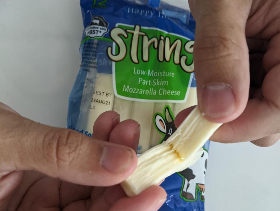 hands pulling Aldi string cheese apart with the blue and green packaging in the background