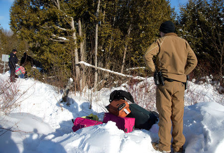 A U.S. border patrol officer looks over with luggage by his feet after a family claiming to be from Sudan crossed the U.S.-Canada border into Hemmingford, Canada, from Champlain in New York, U.S., February 17, 2017. REUTERS/Christinne Muschi