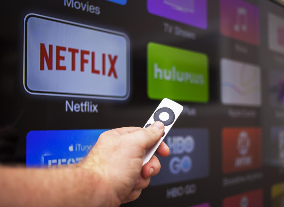 A male hand holds a remote pointed at a screen showing various streaming services. (Source: Getty)