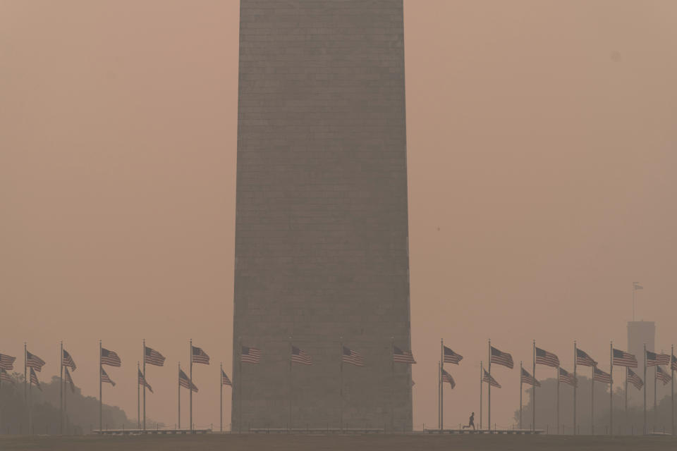 People run at the base of the Washington Monument and a thick layer of smoke covering Thursday, June 8, 2023, in Washington. Intense Canadian wildfires are blanketing the northeastern U.S. in a dystopian haze, turning the air acrid, the sky yellowish gray and prompting warnings for vulnerable populations to stay inside. (AP Photo/Jose Luis Magana)