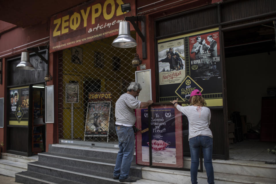 In this Friday May 29, 2020 photo, projector operator Pavlos Lepeniotis, left, and his wife Christina Tsouta, place a poster for an upcoming film outside the Zephyros open-air cinema that specializes in films from past decades in the Petralona district in central Athens. (AP Photo/Petros Giannakouris)