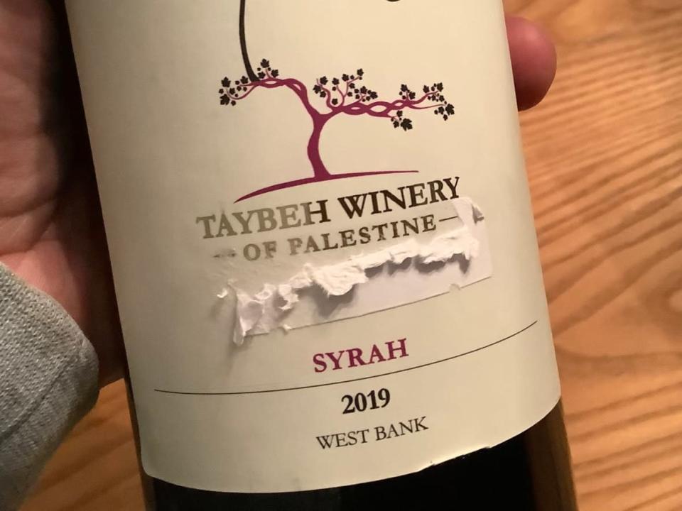 Samer Abdelnour holds a bottle of wine from Taybeh Winery that he bought from the LCBO. It came with a plain white sticker covering the front of the label, placed over the words &#39;of Palestine.&#39; (Submitted by Samer Abdelnour - image credit)