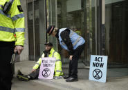 An Extinction Rebellion climate change protester with his hand glued to the floor outside the London Stock Exchange talks to a police officer in the City of London, Thursday, April 25, 2019. The non-violent protest group, Extinction Rebellion, is seeking negotiations with the government on its demand to make slowing climate change a top priority. (AP Photo/Matt Dunham)