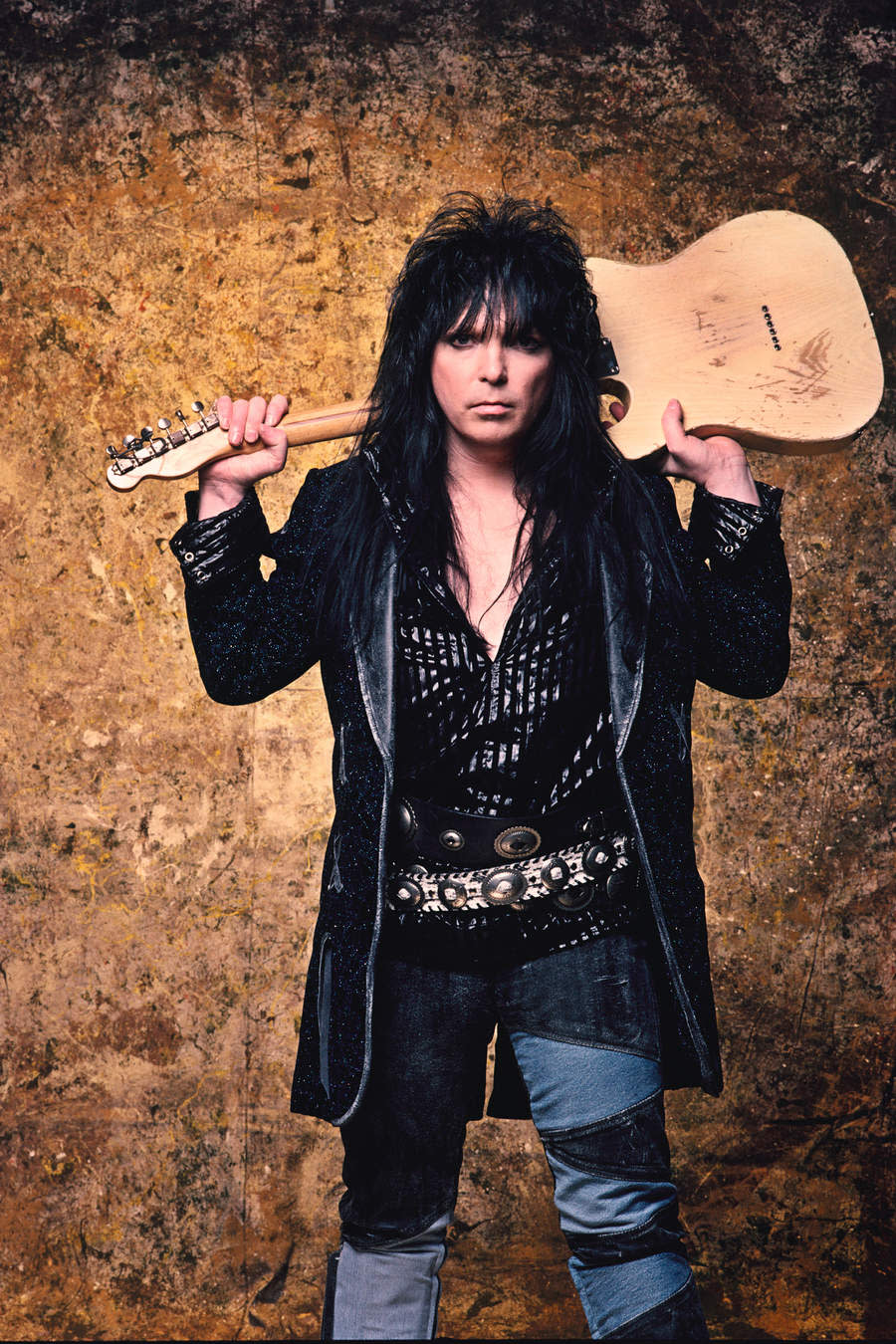 Mick Mars studio portrait, holding guitar behind his head