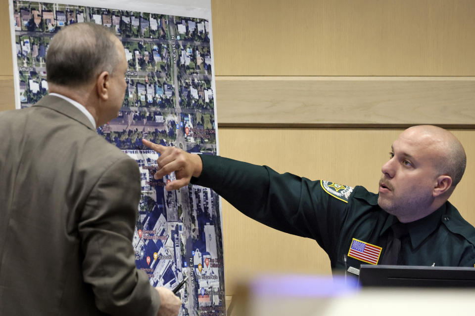 Palm Beach Sheriff's Office Deputy Xavier Pastrana Santiago points on an enlarged photograph to a tree-lined sidewalk, where patients from the Rehabilitation Center at Hollywood Hills were evacuated when the nursing home lost air-conditioning due to a power outage, at the Broward County Courthouse in Fort Lauderdale, Fla., Monday, Feb. 6, 2023. Santiago was a Hollywood Police officer at the time and responded to the nursing home incident. Prosecutors during opening statements accused Jorge Carballo of abandoning his patients, going home after the Rehabilitation Center at Hollywood Hills lost power to its air conditioner during Hurricane Irma. (Amy Beth Bennett/South Florida Sun-Sentinel via AP, Pool)