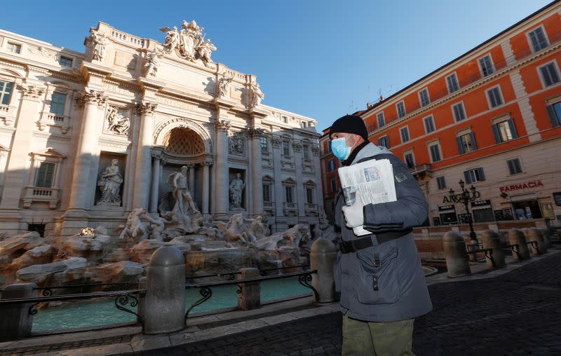 A man wearing a protective face mask walks next to the Trevi fountain, virtually deserted as Italy fights a coronavirus outbreak, in Rome