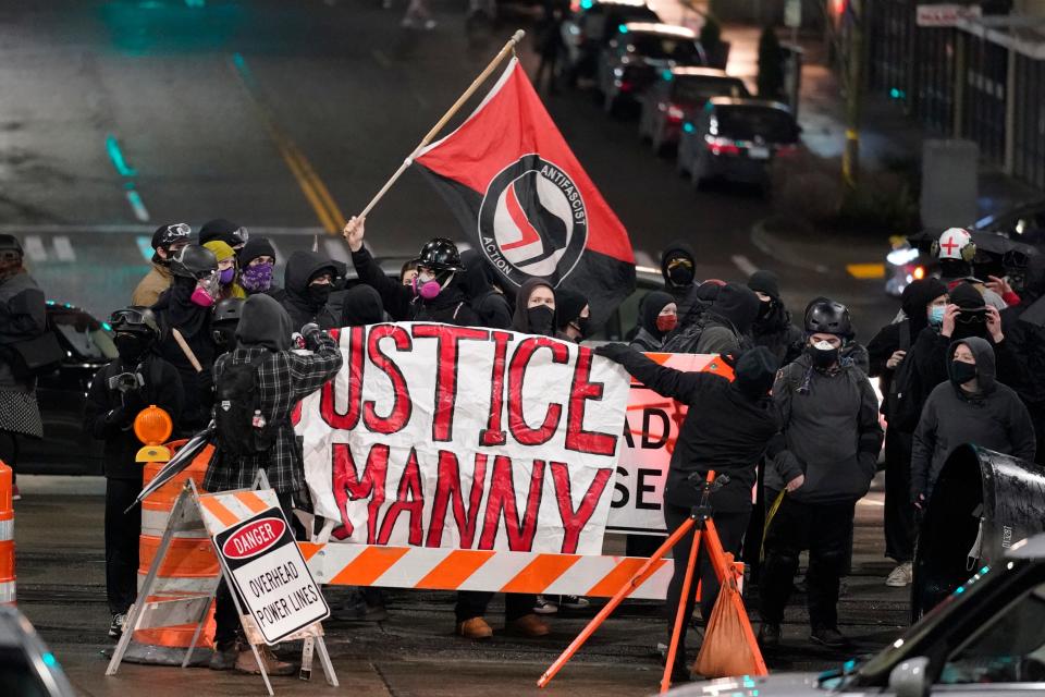 A protester carries a flag that reads "Antifascist Action" near a banner that reads "Justice for Manny," during a protest against police brutality in January 2021 in downtown Tacoma, Washington. The banner is in support of Manuel Ellis, a Black man who died in Tacoma after his airways were restricted by law enforcement officers in March 2020.