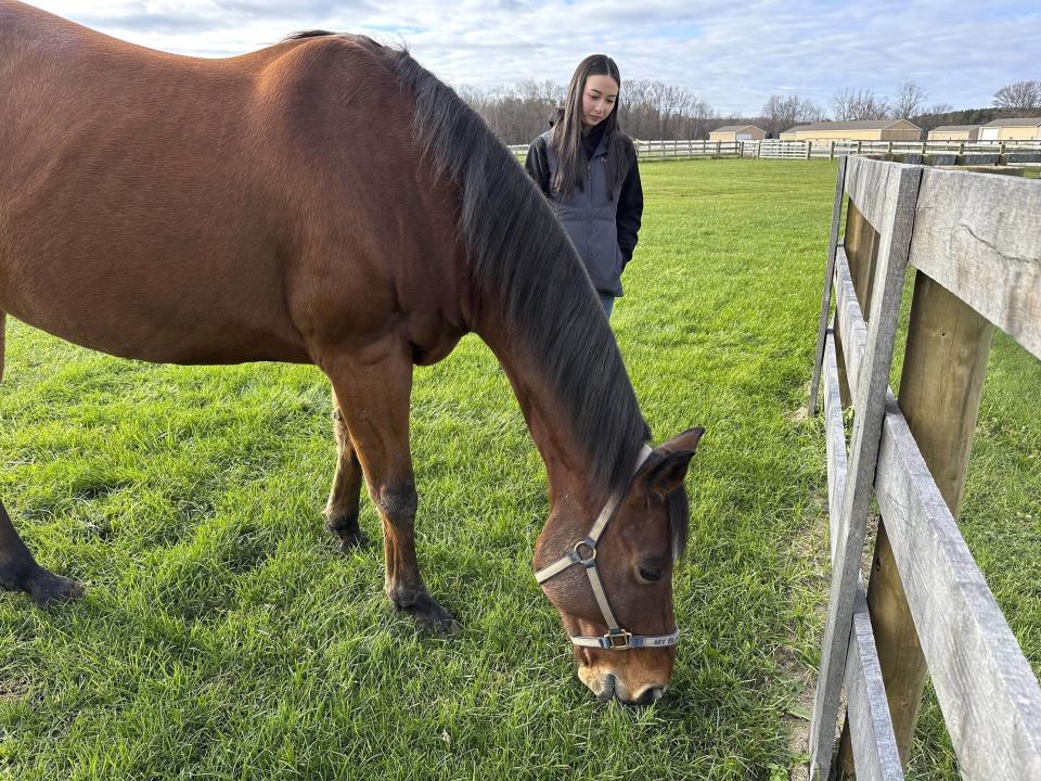 Kylie Ossege watches as her horse, Blaze, grazes in a field at a boarding facility Saturday, Nov. 11, 2023, in Mayfield Township, Mich. Ossege was severely injured in a 2021 mass shooting at Oxford High School and says spending time with Blaze provides her with a measure of comfort. (AP Photo/Mike Householder)