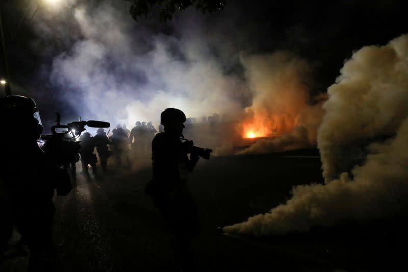 A photojournalist reacts as riot police shot tear gas on the 100th consecutive night of protests against police violence and racial inequality, in Portland, Oregon