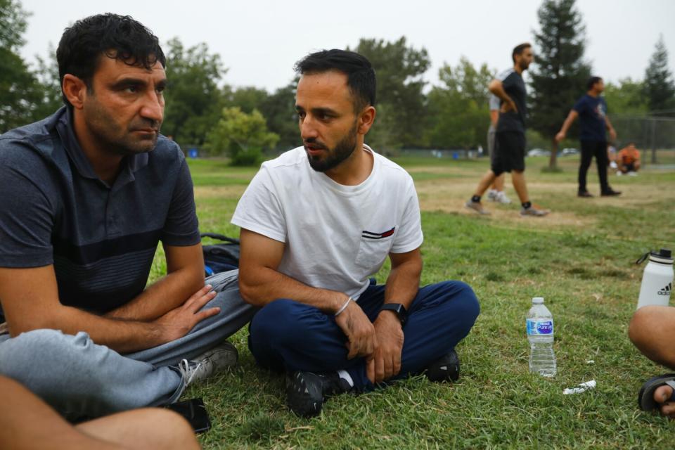 Men sitting cross-legged on the grass while others play in the background