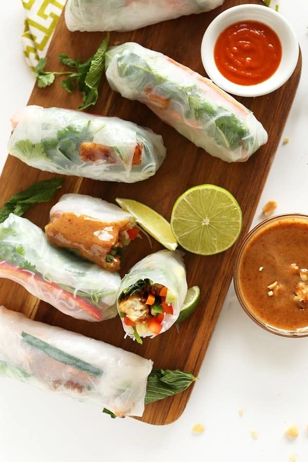 Fresh spring rolls with vegetables and herbs, served with dipping sauces and lime wedges on a wooden board