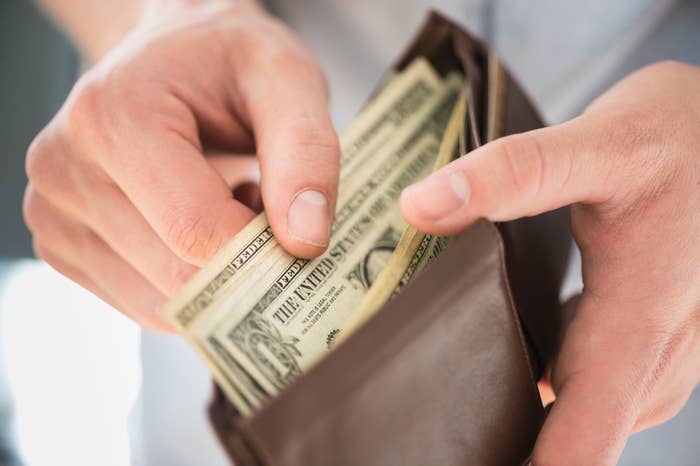 Two hands holding several U.S. dollar bills, being placed in or taken out of a brown wallet