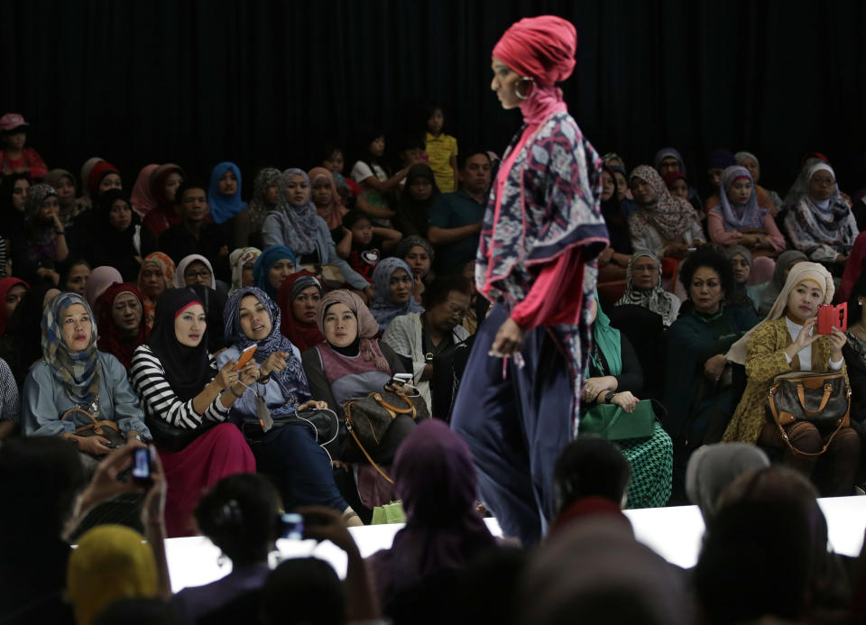 In this Saturday, May 31, 2013 photo, Muslim women react as a model showcases a creation by Indonesian designer Najua Yanti during the Islamic Fashion Fair in Jakarta, Indonesia. The event is part of the Indonesian government's effort to turn the most populous Muslim country into the world's Islamic fashion capital by 2020. (AP Photo/Dita Alangkara)