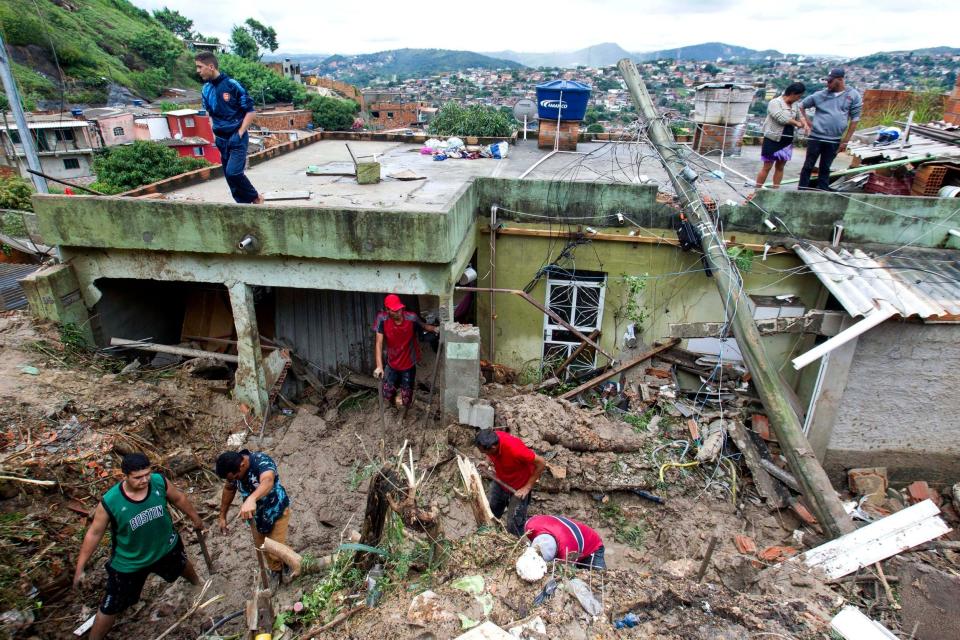 Locals work to clean up mud and debris around houses destroyed by a landslide after heavy rains in Vila Ideal neighbourhood, Ibirite municipality (AP)