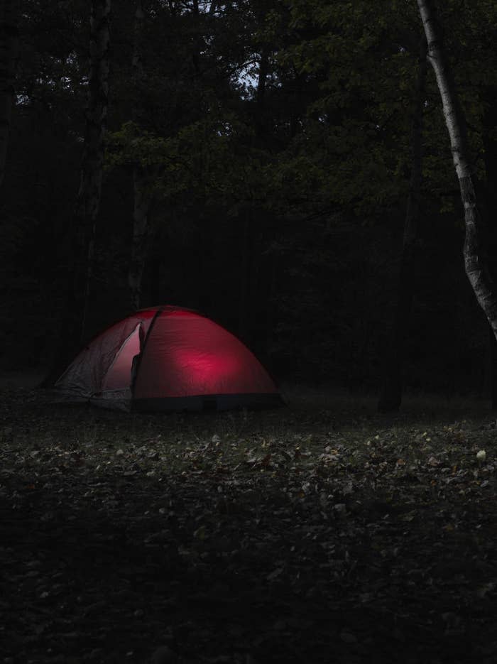 A tent glowing red with dim light sits by itself on a dark night
